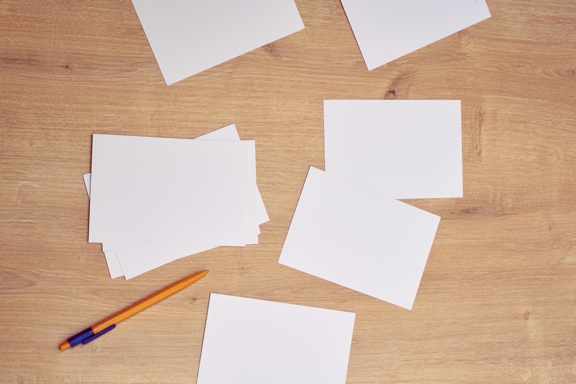 Blank white cards scattered beside a yellow pen on a wooden table.