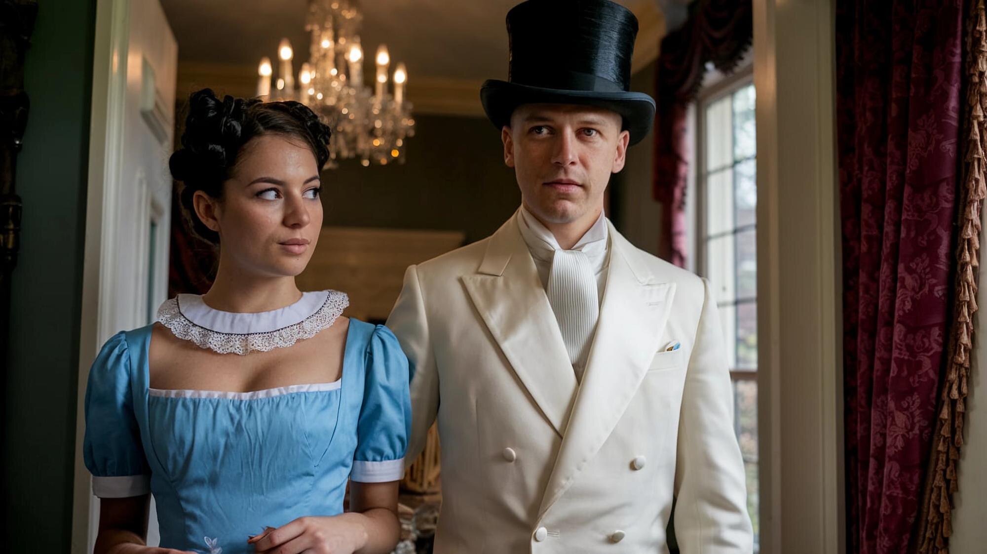 A woman in a blue dress stands beside a man in a white coat and black top hat near a window.